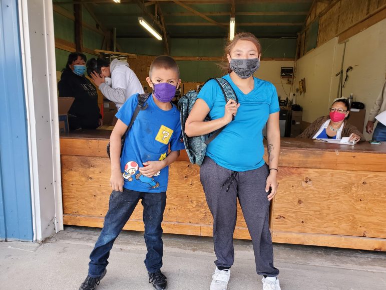 Native American child and adult with backpacks, standing in front of a community center, ready for the new school year.