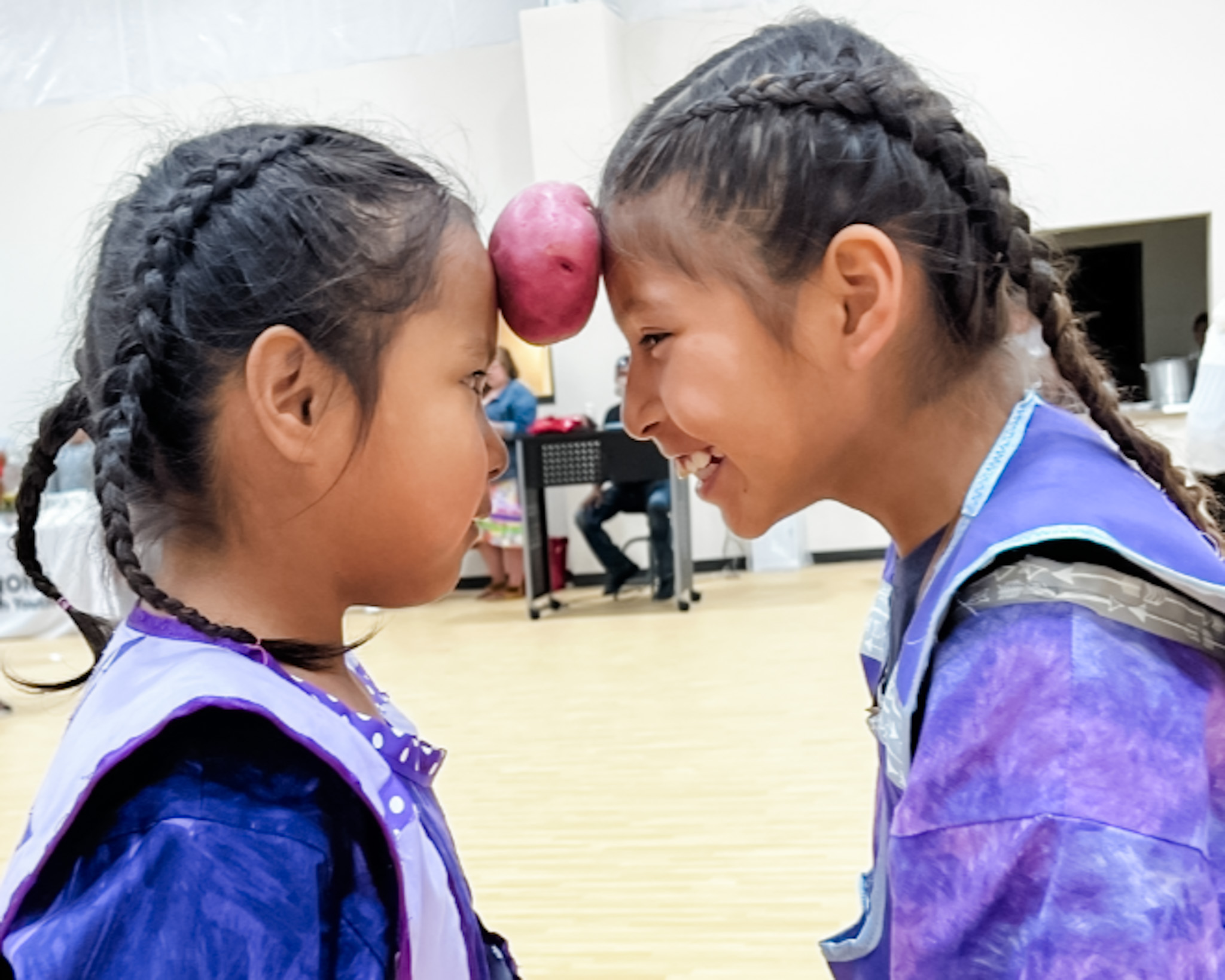 Two girls playing a game with a potato pushed against their foreheads smiling and not worrying about pine ridge reservation poverty.