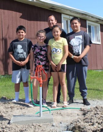 A family is standing next to their water source showcasing one of the water scarcity solutions Running Strong is providing.
