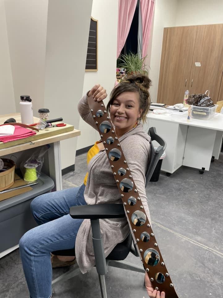 Young woman holding a handmade concho belt during a Lakota crafts class.