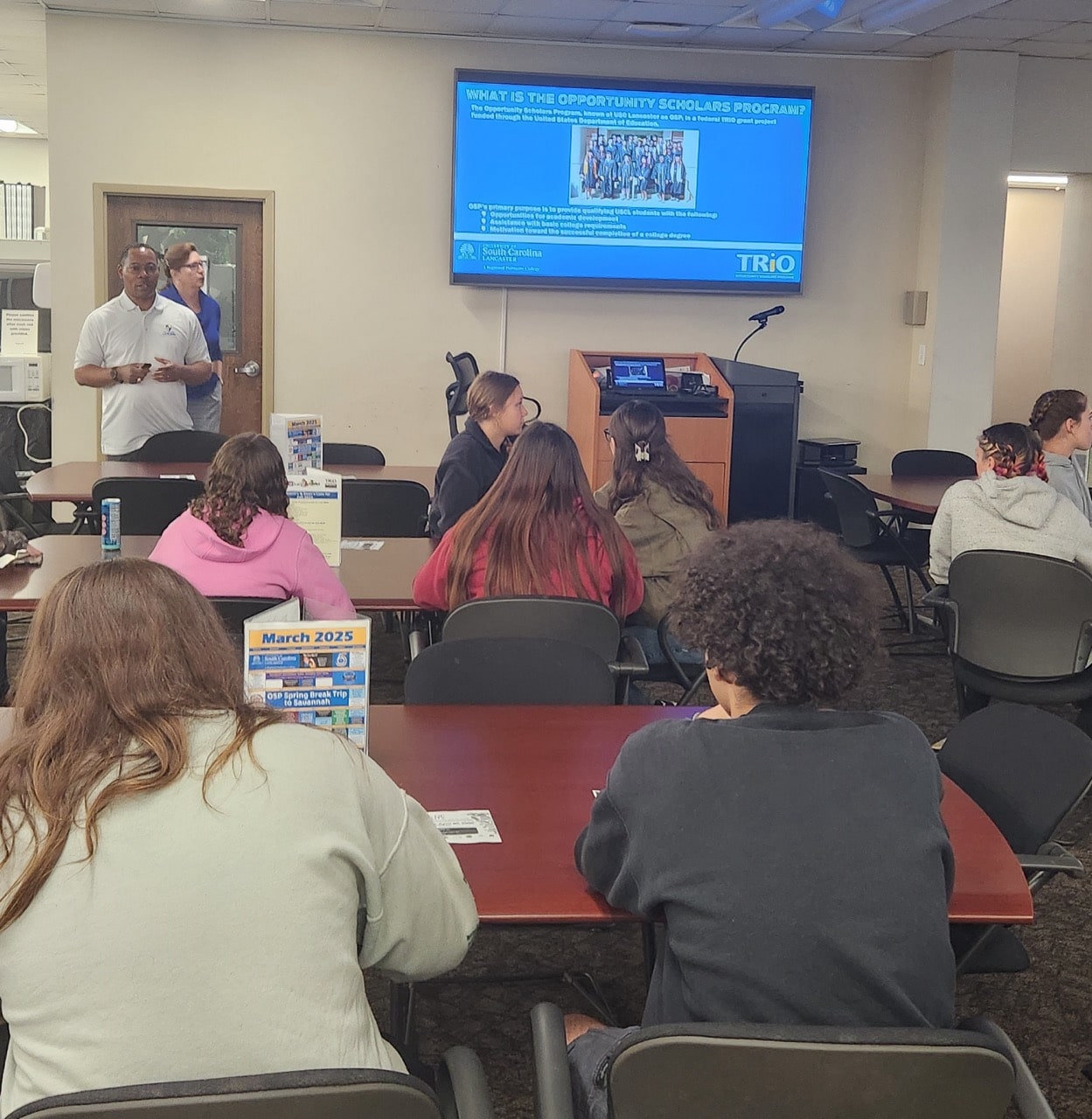 Instructor presenting to small group in classroom using large screen