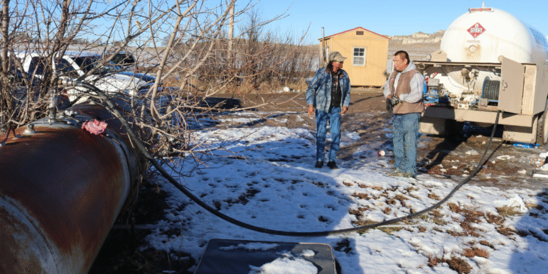 Native American men receiving propane for winter heating in a snowy yard.