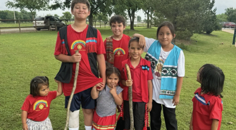 Group of Native youth smiling outdoors in colorful clothing after a program activity.