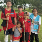 A group of seven Yuchi children of various ages smiling together on a grassy field in Sapulpa, Oklahoma.