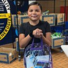Pine Ridge student holding a backpack filled with school supplies at Oyate Ta Kola Ku community center