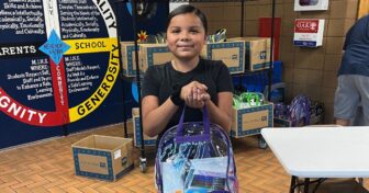 Pine Ridge student holding a backpack filled with school supplies at Oyate Ta Kola Ku community center