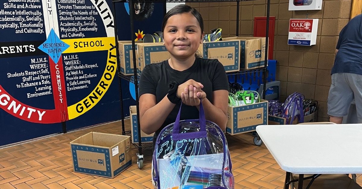 Pine Ridge student holding a backpack filled with school supplies at Oyate Ta Kola Ku community center