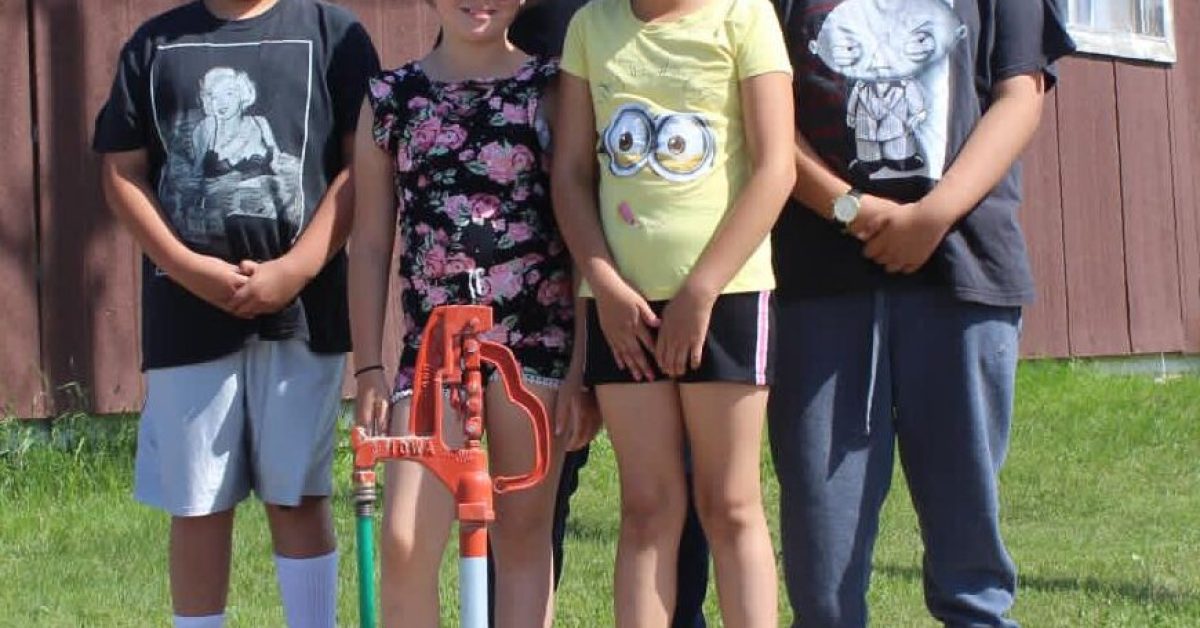 A family is standing next to their water source showcasing one of the water scarcity solutions Running Strong is providing.