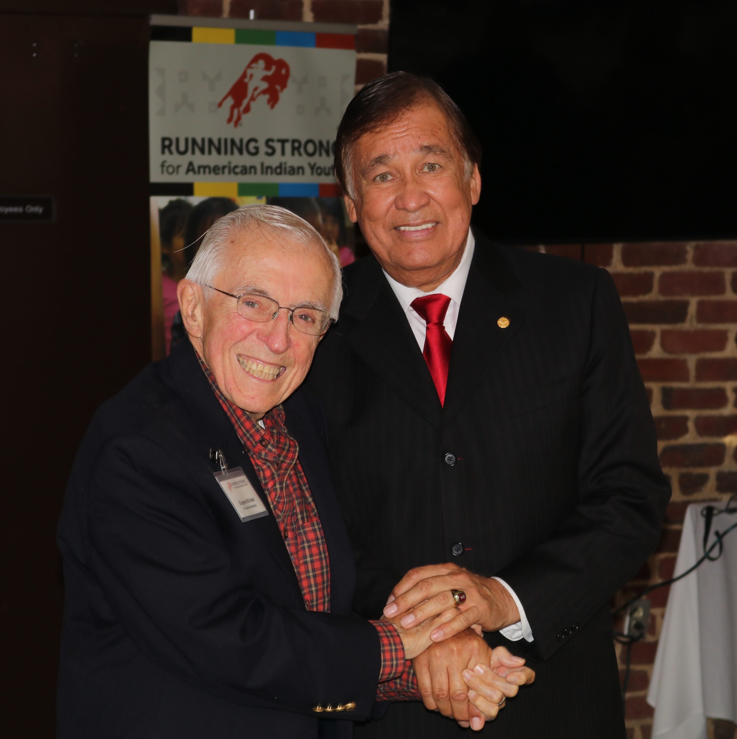 Billy Mills and Gene Krizek smiling and holding hands.