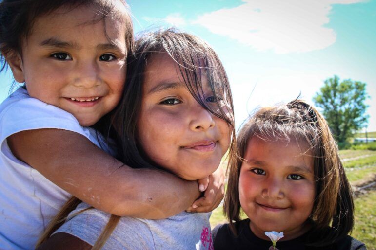 Three smiling young Native American girls posing together outdoors.