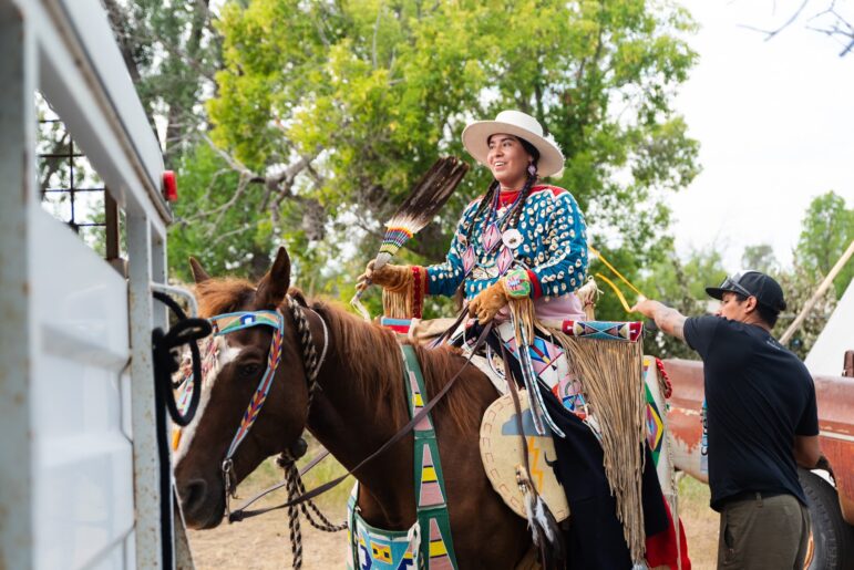 JoRee LaFrance riding in traditional Apsáalooke regalia during a cultural gathering
